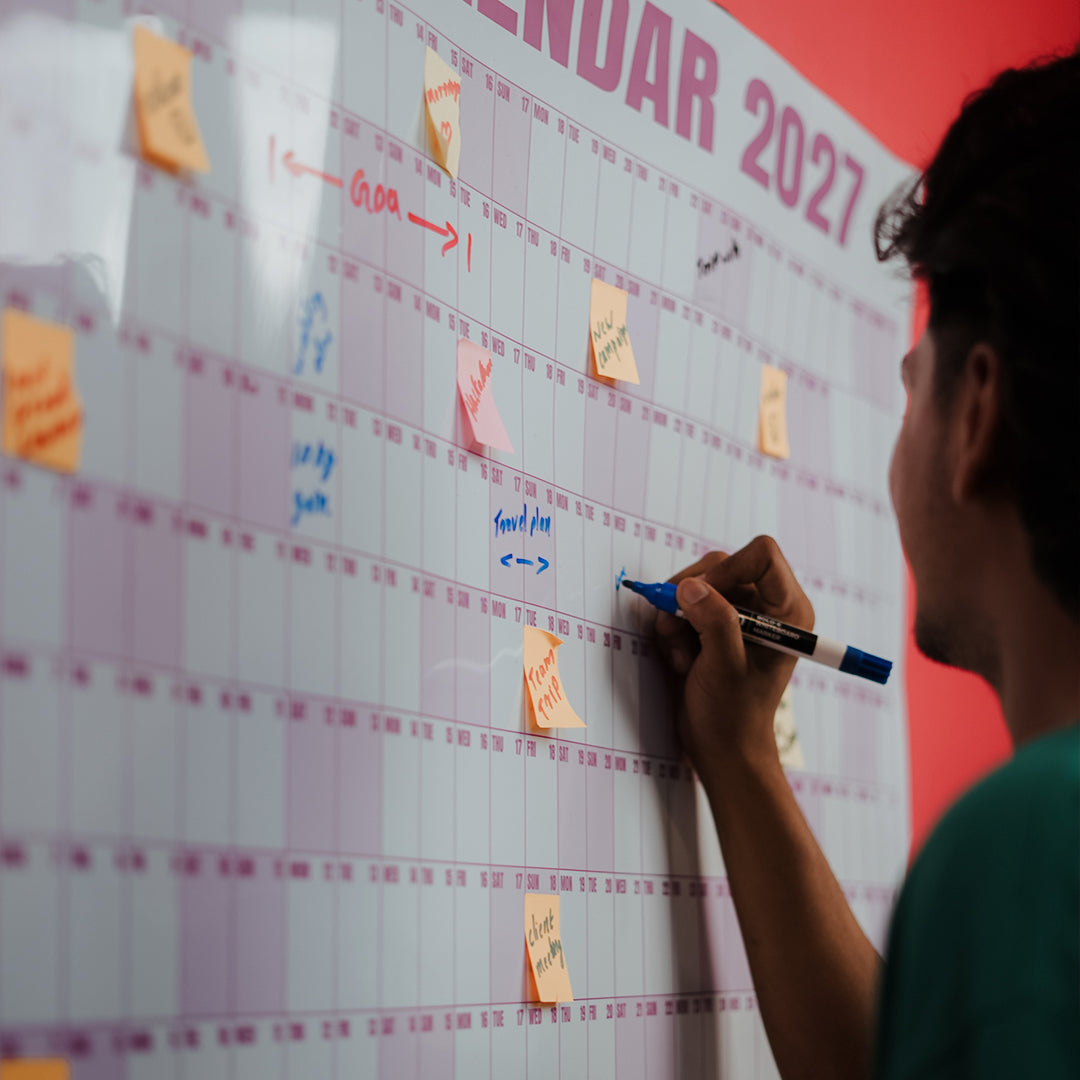 Hand adding a plan to a Rose EPIC Calendar on a red wall