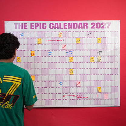Person writing on a Rose EPIC Calendar mounted on a red wall