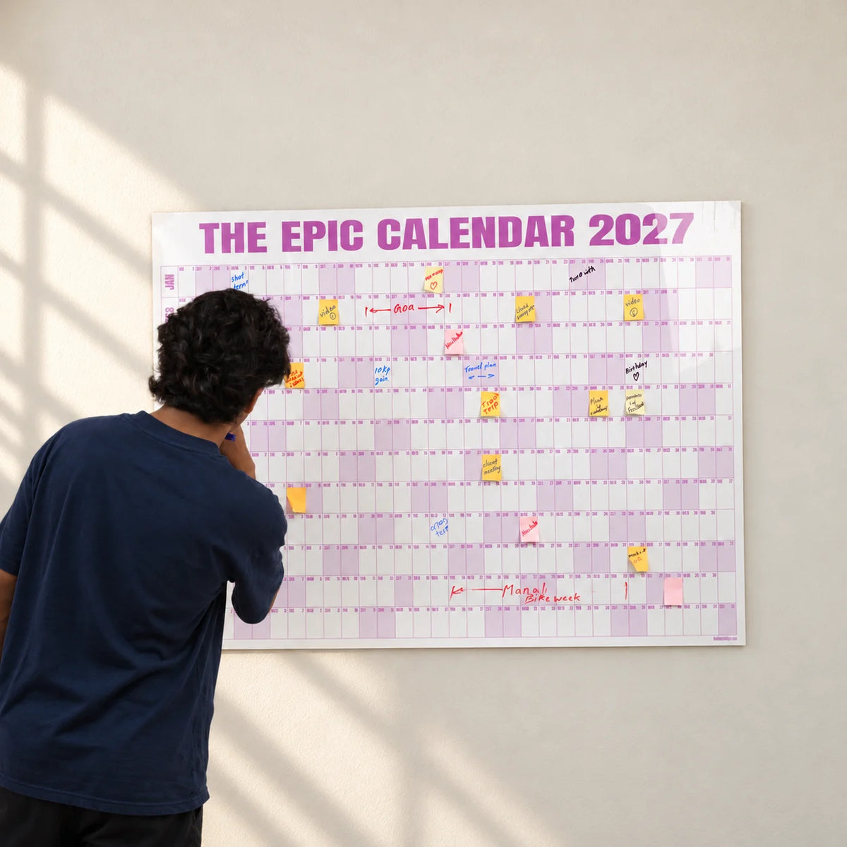 Styled photograph of a young man writing on the 48 by 36 inch Rose EPIC Calendar